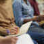 Close-up of group of people sitting on chairs and making notes in notebooks during seminar