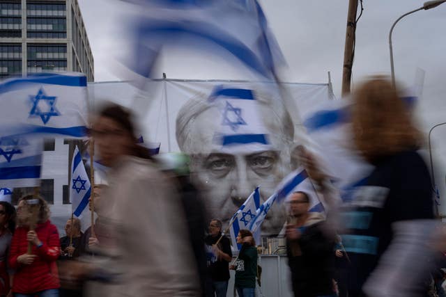 313112d5bad94b5bb4240d654c1717d6-1 Demonstrators walk with Israel’s national flag next to a banner showing Prime Minister Benjamin Netanyahu during a protest in Tel Aviv against plans by his government to overhaul the judicial system
