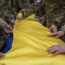 Ukrainian servicemen fold the national flag over the coffin of a comrade during a funeral