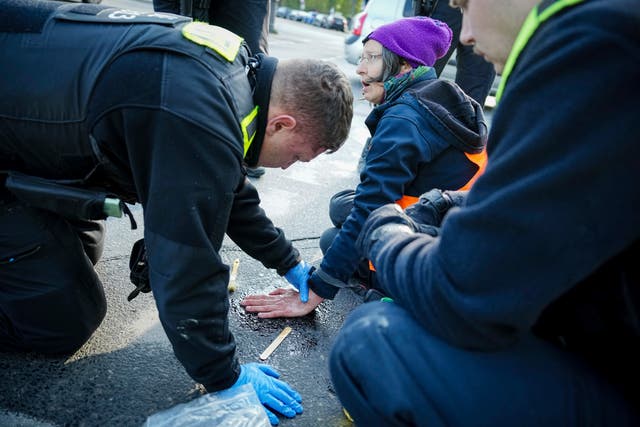 A police officer attempts to remove the hand of a climate activist from the road at Grosser Stern, in front of the Victory Column, in Berlin