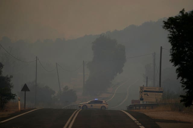 A police car blocks a road as the smoke from the wildfire engulfs the village of Agia Sotira, near Athens