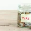 Coins in glass jar with Tips label. Money savings, tips and donation concept, copy space.