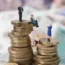 Models of men and women on a pile of coins and bank notes
