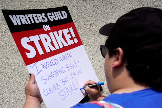 794da57904f44d1b84c419c102694ed9 Isaac Gomez, a captain in the Writers Guild of America West, writes out a message on a sign before a rally in front of Paramount Pictures in Los Angeles