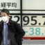 People walk in front of a board showing Japan's Nikkei 225 index