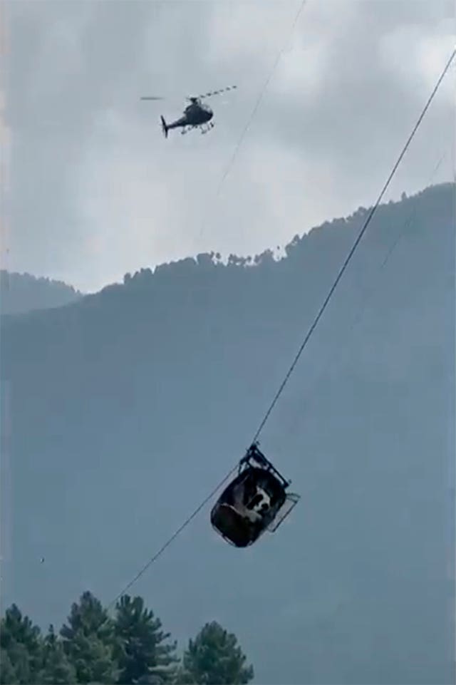 5e56f174a47b40de9cd8da0f82acf2d5 The cable car dangles hundreds of feet above the ground while it is circled by a helicopter
