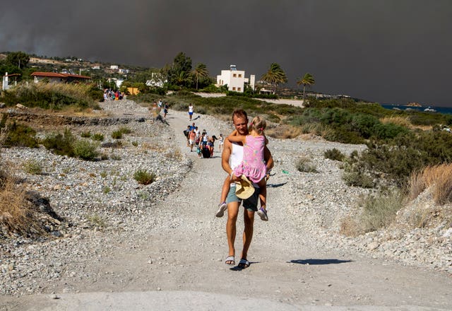 7f0b1240e7424497bf0f3d50126f836f-1 A man carries a child as they leave an area where a forest fire burns on Rhodes