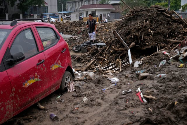 f7236b76786e471ca4e5c1e311260afa A man walks by a damaged vehicle in the aftermath of flood waters from an overflowing river in the Mentougou district on the outskirts of Beijing