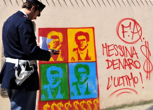 An Italian police officer looks at graffiti, on the perimeter wall of Palermo’s city’s cathedral, portraying Messina Denaro