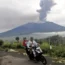 Two people on a motorcycle ride past as Mount Marapi spews volcanic material