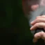 A man vaping with focus on his hand as he holds the e cigarette / vape mod up to his mouth while exhaling vapour