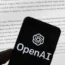 OpenAI logo seen on a mobile phone in front of a computer screen