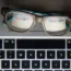 The Google logo reflected in a pair of glasses next to a keyboard