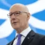 John Swinney making a speech with a Saltire flag backdrop