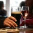 A person's hand holds a Guinness pint glass on a table next to a wine glass