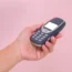 Close up hand holding mobile phone Nokia 3310 isolated on pink background. Female hand holding old used phone Nokia 3310.
