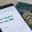 An energy bill on a smartphone next to coins and a £5 note