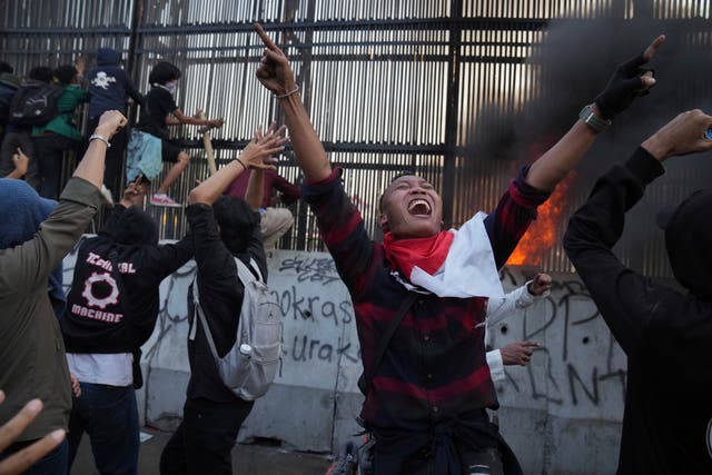 15c0af44dac24275bfcdada17d0c9819 A protester in the foreground raises his arms in the air and shouts as others behind him try to scale a fence
