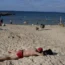 A man in red trunks lies face down on a sandy beach