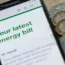 An online energy bill displays on a phone screen, with coins and notes sitting beside the handset