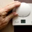 An elderly woman adjusts her heating thermostat