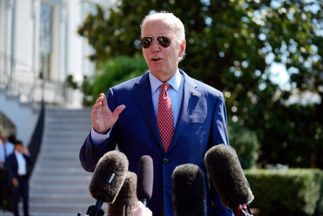 a0af2ea032bb4233a02483709c9bc0c6 Joe Biden in sunglasses, with one had raised as he speaks in front of a number of microphones
