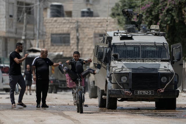 b91b0b6a427747d0b5857d32a1fa1099 A youth rides his bicycle past an Israeli armoured vehicle