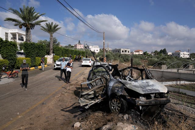 ba880d92277a4a76882f9d6e49262f54 People gather around a destroyed car