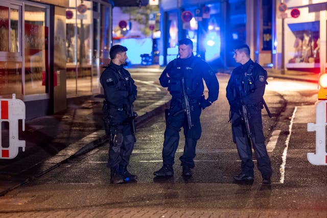 e5474f6dcd3f440ba3e6b364ae590477 Three officers with guns stand in the street