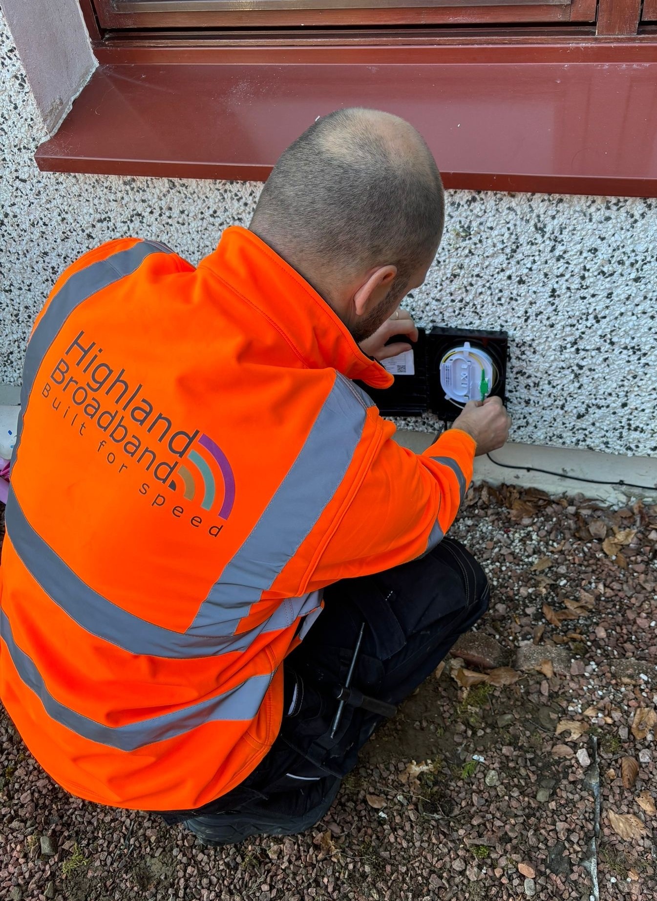 f3a8486d-4d8e-46cb-a400-a2c4632b764d Highland Broadband engineer installing equipment on the side of a building