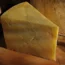 Wedge of mature cheddar cheese on board with whole cheese and bread in background